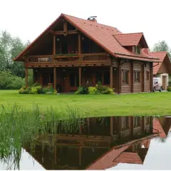 Piękny dom z bali z czerwonym dachem, odbijający się w stawie. Zastanawiasz się, ile kosztuje dom z bali?